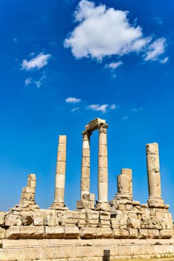 Ziyaretçiler Ürdün 'ün Amman kentindeki Hisar' daki antik taş kalıntılarını açık mavi gökyüzünün altında keşfediyorlar. Sitede birkaç uzun sütun yer alıyor.