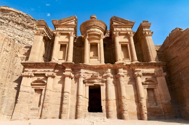 Visitors explore the Monastery at Petra in Jordan. This historical site shows ancient architecture carved from rock.