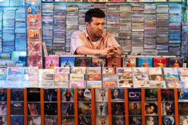 Adamın biri Marakeş 'te bir markette duruyor ve müşterilere çeşitli CD' ler satıyor. Renkli görüntüde birçok müzik albümü yer almaktadır..