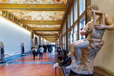 Ziyaretçiler Floransa 'daki Uffizi Galerisi' nin Birinci Koridoru 'nda yürürken ayrıntılı tavan altındaki sanat ve heykellere bakıyorlar..