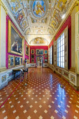 Palazzo Pitti 'deki Palatine Galerisi' nde gezen ziyaretçiler duvarlardaki sanat eserlerini ve dekoratif tavanı görüyorlar. Oda zengin dekorasyon ve ayrıntıları gösteriyor..