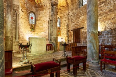 Ziyaretçiler İtalya 'nın Palermo kentindeki Cappella di San Cataldo' yu ziyaret ediyorlar. Mekanda sütunlar, bir taş sunak ve tahta sandalyeler var..