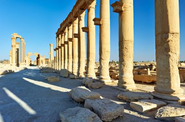 Ziyaretçiler büyük sütunlarda yürürler ve Palmyra 'daki anıtsal kemeri görürler. Harabeler tarihi bir uygarlığın hikayelerini anlatıyor..