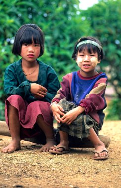 İki çocuk birlikte Myanmar 'da oturuyor, doğanın tadını çıkarıyorlar. Geleneksel kıyafetler giyerler ve kameraya gülümserler..