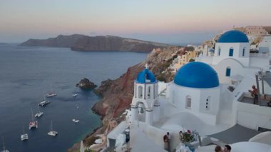 İkonik mavi kubbeli kiliseler ve güneş doğarken çarpıcı kaldera ve Ege Denizi manzaralı Oia, Santorini, Yunanistan 'daki beyaz binalar.