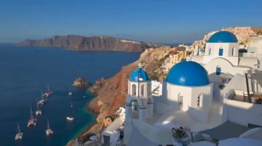 İkonik mavi kubbeli kiliseler ve güneş doğarken çarpıcı kaldera ve Ege Denizi manzaralı Oia, Santorini, Yunanistan 'daki beyaz binalar.