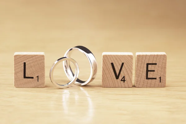 Le mot amour avec des anneaux de mariage et des morceaux de scrabble Photo De Stock