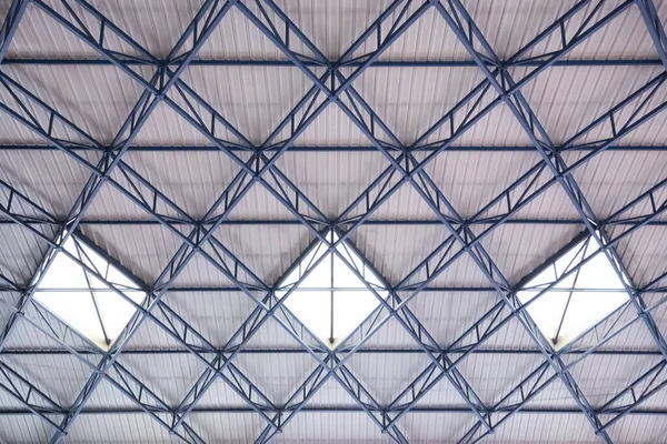 Abstract image of an industrial roof with three skylights between the blue beams and the white roof.
