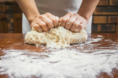 Un dolu ahşap bir masada ekmek yoğuran bir kızın ellerinin ayrıntıları..