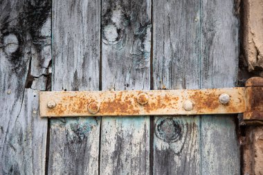Eski ahşap bir kapının üzerindeki paslı menteşe maviye boyanmış. Metal ve ahşabın farklı dokularının ayrıntıları..