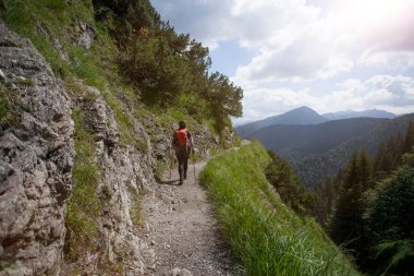 Kızıl sırt çantasıyla Bavyera Alplerinde yürüyüş yapan bir kadın.