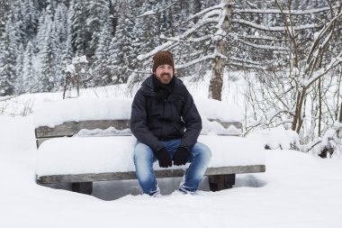 Genç adam karlı bir bankta oturuyor