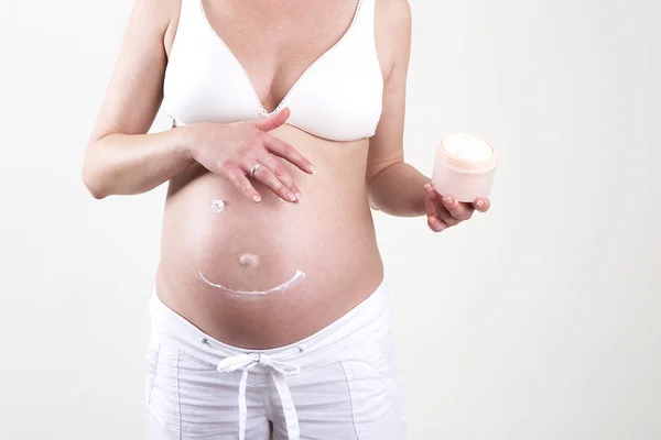 Hamile kadın Smiley krem ile onun karnına koyarak — Stok fotoğraf