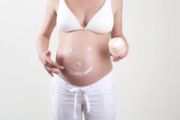 Schwangere setzt Smiley mit Creme auf ihren Bauch — Stockfoto