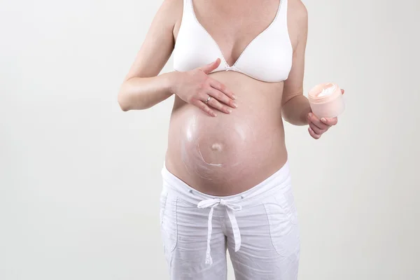 Zwangere vrouw zetten crème op haar buik — Stockfoto