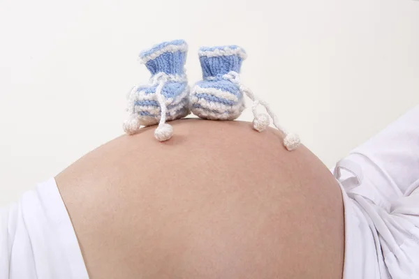 Schwangere mit blauen Babyschuhen am Bauch — Stockfoto