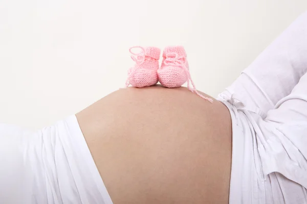 Mulher grávida com sapatos de bebê rosa em sua barriga — Fotografia de Stock