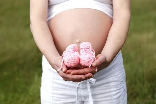 Hamile kadın açık pembe Bebek Patikleri elleri ile — Stok fotoğraf