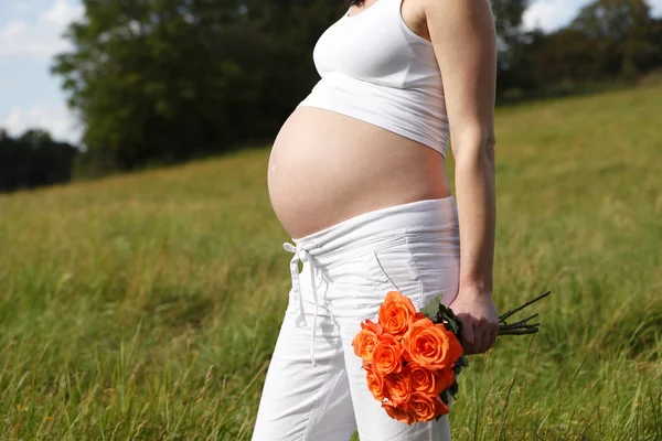 Беременная женщина на улице с оранжевыми тюльпанами в руках — стоковое фото