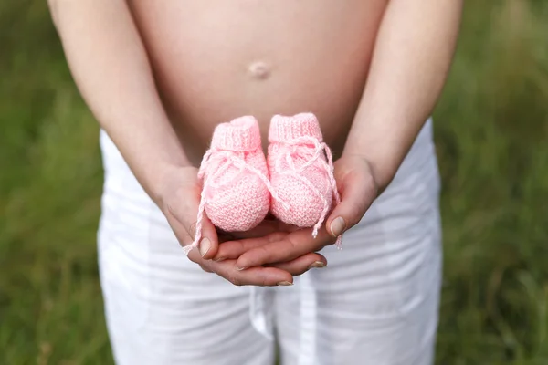 Zwangere vrouw buiten met roze baby schoenen in haar handen — Stockfoto