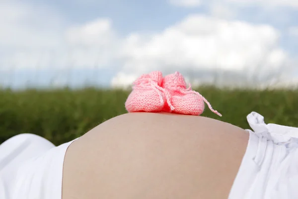 Mulher grávida com sapatos de bebê rosa em sua barriga — Fotografia de Stock