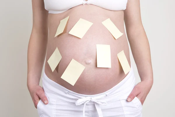 Zwangere vrouw met een heleboel gele etiketten op haar buik — Stockfoto