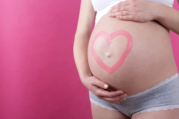 Close-up de uma mulher grávida com coração rosa na barriga — Fotografia de Stock