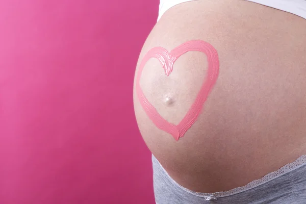 Close-up de uma mulher grávida com coração rosa na barriga — Fotografia de Stock