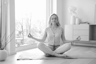 Genç ve güzel bir kadın büyük pencerenin yanında yoga yapıyor.