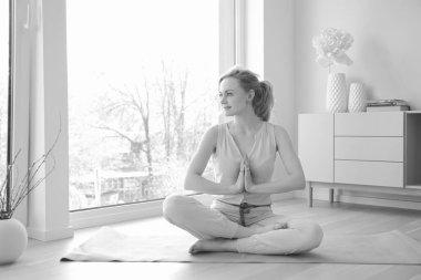 Genç ve güzel bir kadın büyük pencerenin yanında yoga yapıyor.