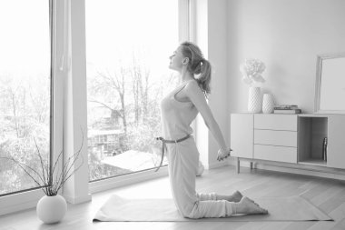 Genç ve güzel bir kadın büyük pencerenin yanında yoga yapıyor.