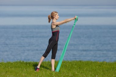 Genç bir kadın sabah deniz kenarında egzersiz yapıyor.