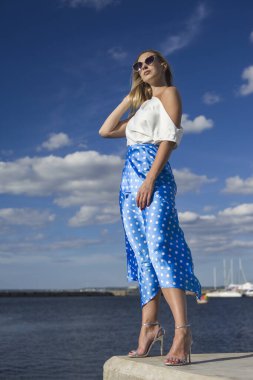 Deniz kenarındaki genç, narin kadın. Kıyafetler içinde poz veriyor.