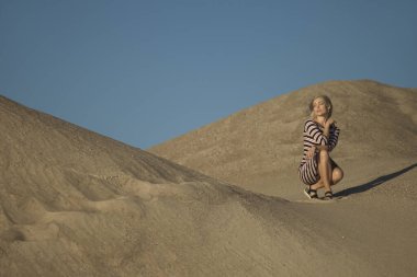 Genç bir kadın kumlu dağda elbise giymiş poz veriyor.