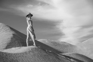 Genç bir kadın kumlu dağda elbise giymiş poz veriyor.