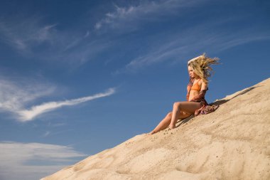 Genç bir kadın kumlu dağda elbise giymiş poz veriyor.