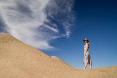 Genç bir kadın kumlu dağda elbise giymiş poz veriyor.