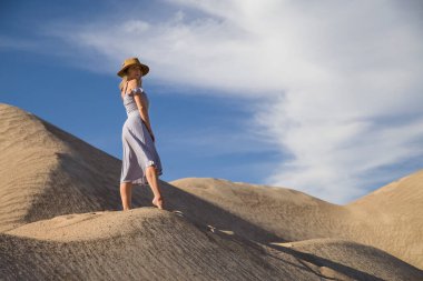 Genç bir kadın kumlu dağda elbise giymiş poz veriyor.