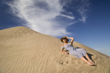 Genç bir kadın kumlu dağda elbise giymiş poz veriyor.
