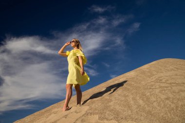 Genç bir kadın kumlu dağda elbise giymiş poz veriyor.