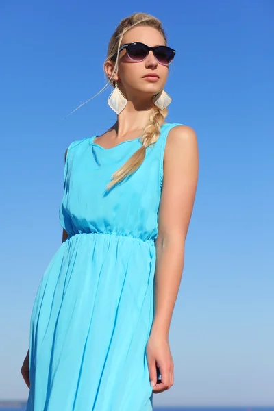 Chica en un vestido azul y gafas de sol en el fondo del cielo —  Fotos de Stock