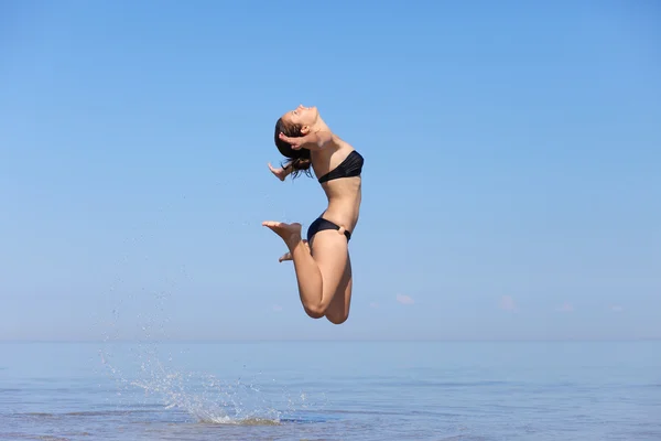 Beautiful young girl jumping on sea — Stock Photo, Image