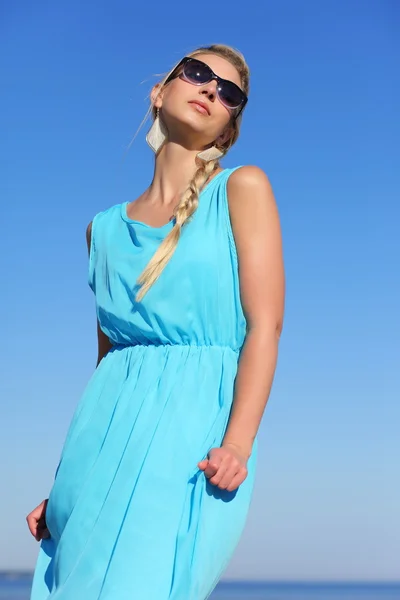 Chica en un vestido azul y gafas de sol en el fondo del cielo —  Fotos de Stock