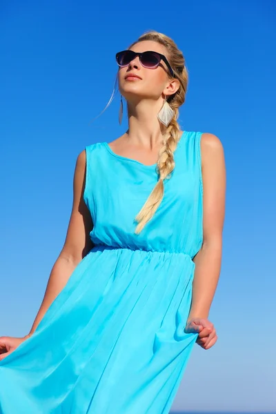 Chica en un vestido azul y gafas de sol en el fondo del cielo —  Fotos de Stock