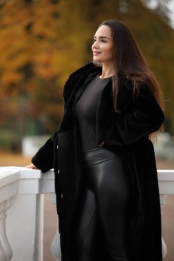 Sonbaharda dışarıda poz veren siyah ceketli zarif bir kadın.