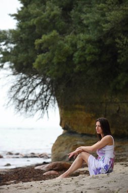 Genç bir kadın kumsalda sahil kenarında oturuyor.