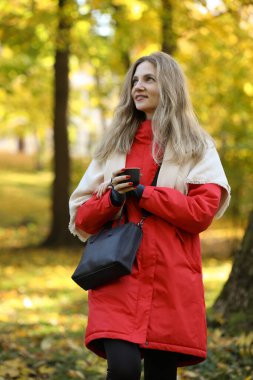 Parlak ceketli güzel bir kadın Sonbahar parkında yürüyüş yapıyor.