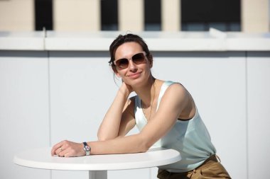 Güneş gözlüklü, kendine güveni tam bir kadın çatıdaki kafede rahatça oturuyor.