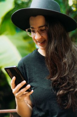 Cep telefonu kullanan, gözlüklü, siyah şapkalı bir kadının portresi..