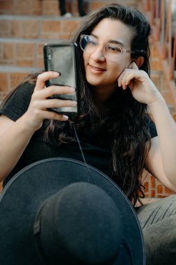 Cep telefonu kullanan, gözlüklü, siyah şapkalı bir kadının portresi..